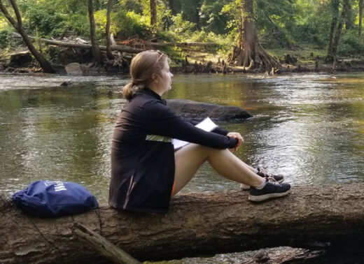 student looking at nature next to river