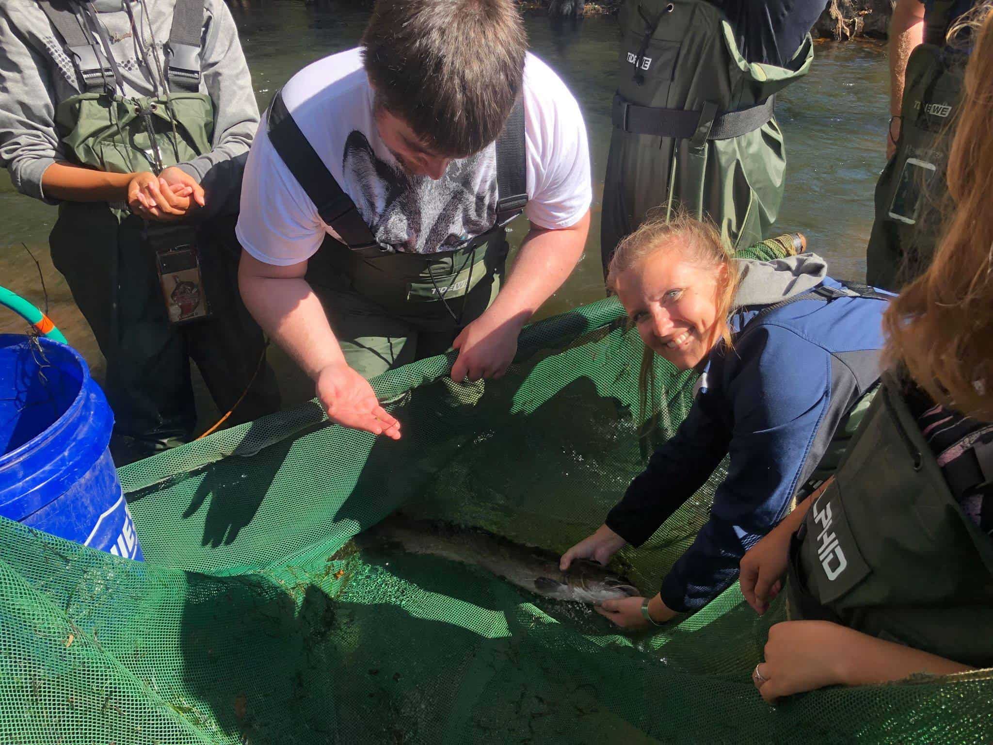 biology students holding fish in river doing research