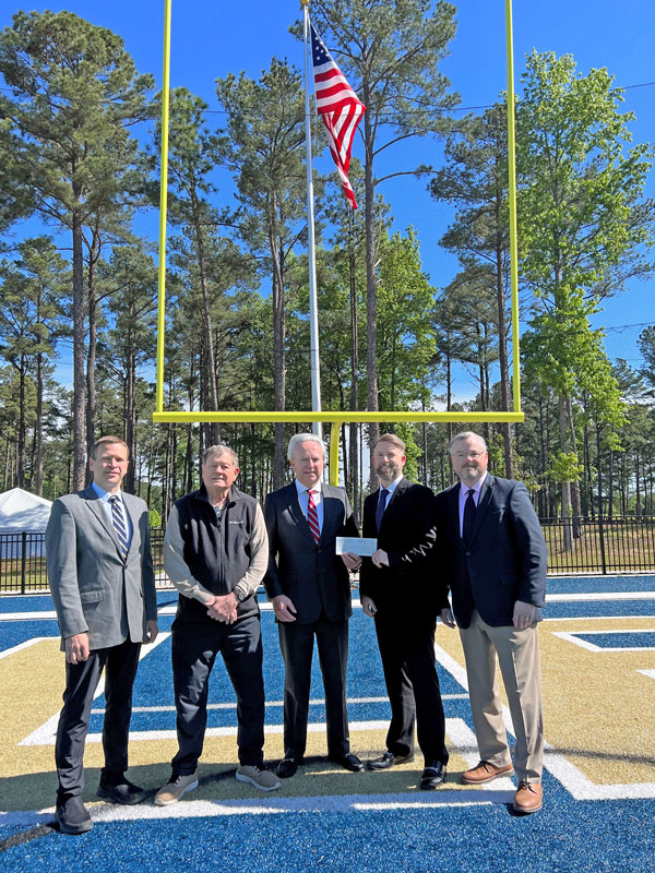 Group stands on NC Wesleyan's turf field in front of goal post for check presentation