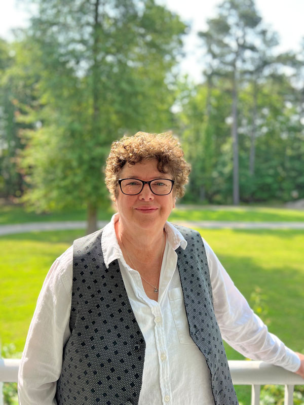 Middle-aged white female with glasses stands in front of white porch railing.