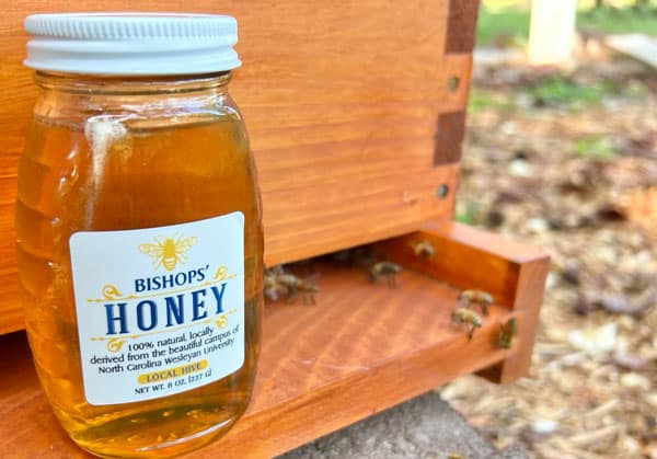 A jar of honey sits on the ledge of a bee hive.