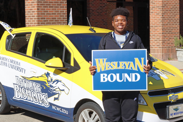 student in front of car with wesleyan bound sign